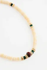 Collar de cuentas de concha de río en color crema, intercaladas con pequeñas piezas metálicas doradas, cuentas de vidrio verde y una cuenta central de vidrio en tono borravino.