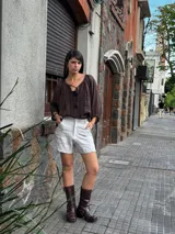 Short de lino en color celeste, con diseño de tiro alto, cierre frontal con botón a la vista y costuras decorativas verticales en el frente.