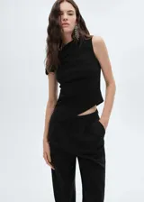 Top negro de diseño asimétrico con escote off-shoulder y detalles drapeados. Es una prenda sin mangas, entallada y confeccionada en tejido fluido.