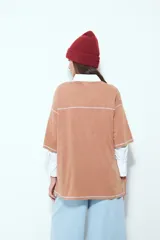 Remera de manga corta color marrón con efecto desgastado, corte oversize y costuras a la vista en color blanco. Presenta cuello redondo con cuello polo blanco superpuesto y mangas largas a rayas horizontales marrones y blancas por debajo.