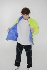 Campera puffer reversible de corte holgado, con cuello alto y cierre frontal. Un lado es de color azul vibrante con detalles en verde lima en el cierre y el interior, y el otro lado es de color negro.