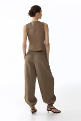 Pantalón de sarga de tiro alto, color marrón, con diseño de piernas globo, pinzas y puños abotonados con frunces. Cuenta con bolsillos laterales discretos y cierre frontal con botón y corchetes ocultos.