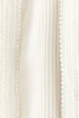 Pantalón oversized de tiro bajo color blanco crudo, confeccionado en viscosa con alforzas, ribetes de encaje, cordón de ajuste y ribete de volado en la cintura.