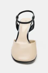 Zapato de tacón alto destalonado, fabricado en piel combinada en tonos beige y negro. Presenta punta redonda, tacón fino de 10 cm y tira elástica ajustable en el talón.