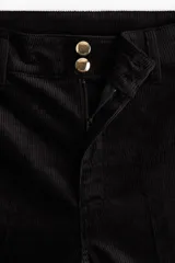 Pantalón de pana de algodón color negro, de tiro alto, con pliegues delanteros y traseros. Cierre con dos botones dorados, bolsillos traseros abiertos y piernas rectas.