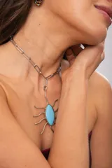 Collar corto de cadena de eslabones plateados con un gran dije colgante en forma de insecto o araña de metal plateado, con una piedra central ovalada de cristal en tono celeste.