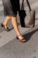 Sandalias de taco cuadrado medio, con base y talón en gamuza color tostado. Presenta una tira frontal de múltiples bandas doradas y una pulsera al tobillo con hebilla metálica.