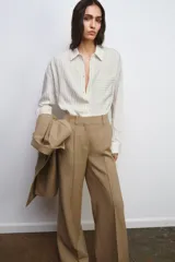 Camisa fluida de corte oversize confeccionada en mezcla de viscosa, con diseño de rayas verticales finas en tono beige sobre fondo blanco. Presenta cuello solapa, cierre frontal con botones, manga larga con puños y un bolsillo de plastrón en el pecho.