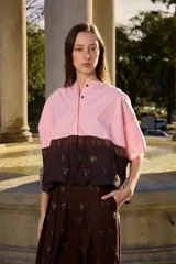 Camisa de manga corta con botones en la delantera, diseño bicolor con parte superior rosada y parte inferior marrón con bordados delicados, y ruedo ajustable.