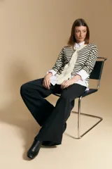 Cárdigan de tejido de punto a rayas horizontales beige y blanco, con escote en V y un lazo ancho anudado al frente. Se lleva sobre una camisa blanca de cuello abotonado con puños anchos.