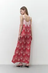 Maxi vestido con breteles finos, corte recto y estampado floral en tonos rojo y blanco sobre fondo rosa pálido.