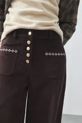 Pantalón de pana de corte wide leg, color marrón oscuro, con calce relajado y detalle de bordado en el borde de los bolsillos delanteros.