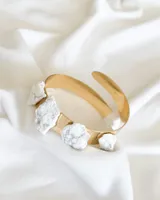 Brazalete rígido dorado con incrustaciones de piedras blancas irregulares.