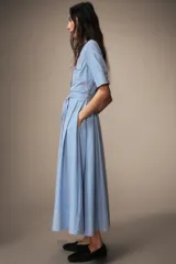 Vestido midi de algodón con estampado de rayas verticales, cuello solapa, manga corta con puños y cierre frontal de botones. Presenta bolsillos con solapa en el pecho y un cinturón de la misma tela para ajustar la cintura.