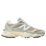 Championes New Balance modelo 9060, con diseño robusto y moderno. Presentan una combinación de tonos beige y gris, con paneles de gamuza y malla. Incluyen el logo 'N' característico en los laterales y una suela gruesa con tecnología de amortiguación.