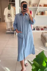 Vestido camisero midi celeste de lino con cuello clásico, manga francesa, cierre frontal con botones, bolsillos laterales y aberturas laterales en el ruedo.