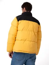 Campera puffer Caterpillar de diseño bicolor en amarillo y negro, con cierre frontal completo, cuello alto y bolsillos laterales con cierre. Presenta el logo de la marca estampado en el pecho y puños ajustables.