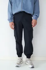 Pantalón cargo tipo jogger color negro, con bolsillos laterales con solapa, cintura con cierre y botón, y puños elásticos en los tobillos.