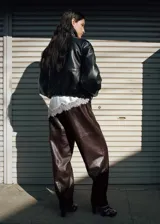 Chaqueta de estilo bomber color negro, confeccionada en 100% piel ovino con acabado de napa y diseño oversize. Cuenta con cuello alto envolvente, manga larga con puños ajustables, cierre delantero oculto con botón magnético y forro interior de poliéster.