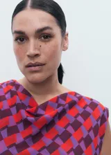 Blusa sin mangas con cuello drapeado, confeccionada en tejido fluido con estampado geométrico en tonos rojos y violetas.