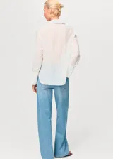 Camisa de corte recto y diseño clásico con cuello camisero, manga larga con puños abotonados y cierre frontal de botones ocultos. Presenta parches decorativos sutiles en la parte frontal.
