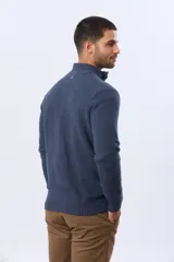 Buzo tejido texturado color verde oscuro, con cuello alto y cierre parcial de tres botones. Tiene mangas largas y un pequeño detalle de etiqueta marrón en el dobladillo inferior.