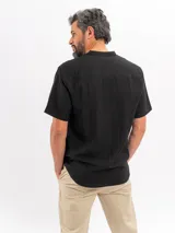 Camisa de manga corta color beige, con cuello mao, bolsillo ojal en el pecho y cierre frontal parcial con botones.