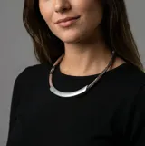 Collar de diseño minimalista con una pieza central curva de metal plateado mate y cordón trenzado con textura tipo piel de serpiente en tonos rosados y oscuros.