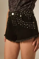 Short de denim negro de tiro medio y calce ajustado, con dobladillo desmechado y detalle de tachas metálicas en forma de estrellas, rombos y esferas en la parte frontal y bolsillos.