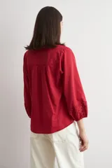 Blusa blanca de corte holgado con cuello mao y escote en V. Presenta detalles de bordado calado en el pecho y en los puños de las mangas tres cuartos.