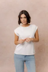 Remera de algodón color blanco, con cuello redondo y mangas cortas con dobladillo vuelto. Presenta un corte relajado y un pequeño aplique metálico en el ruedo.