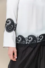 Blusa color marfil de seda con incrustaciones de cruni negro, mangas amplias y cuello cerrado con abertura.