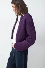 Campera tipo bomber de pana, color violeta, con cuello redondo, cierre frontal con cremallera y puños y bajo elásticos.