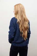 Buzo de punto color gris claro con motas oscuras, escote en V y mangas largas.