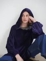 Buzo tipo canguro oversize de tela plush, color azul claro. Presenta capucha, cierre frontal parcial con cordón turquesa y bolsillos canguro frontales. Las mangas son largas y abullonadas con puños ajustados.