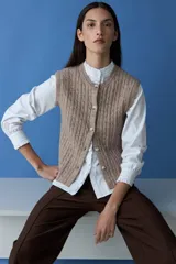 Chaleco de punto con textura acanalada, color tostado melange, con cuello redondo y cierre frontal de botones.