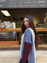 Sweater de punto con diseño de ochos y estilo patchwork, combinando paneles en colores terracota, marrón y beige. Presenta cuello redondo, mangas largas y costuras decorativas a la vista.