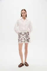 Minifalda de algodón blanca con diseño bordado en tonos marrones que incluye motivos de palmeras y flores.