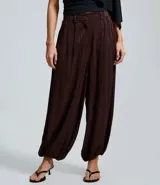 Pantalón de corte aladino confeccionado en viscosa y poliéster, con diseño de rayas verticales y acabado con leve transparencia. Presenta cintura alta, trabillas para cinturón y puños elásticos en el dobladillo.