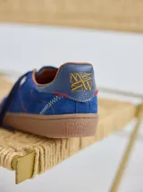 Championes de cuero color tostado con detalles metalizados y pespuntes decorativos en verde y azul. Cuentan con cordones marrones y suela de goma texturizada.