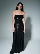 Vestido largo de fiesta, color negro, con diseño strapless y detalle de flores aplicadas en el escote. Confeccionado en tejido cubierto de lentejuelas verticales.