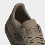 Zapatillas Adidas Handball Spezial de corte bajo, con parte superior de ante en tono beige claro y tres franjas laterales en verde oliva. Presentan puntera en T y suela de goma color café. La inscripción "SPEZIAL" se encuentra en el lateral en color oscuro.