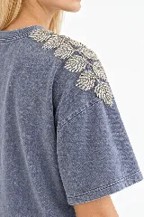 Remera oversize de algodón con acabado stonewash, color gris azulado, manga corta y cuello redondo. Cuenta con apliques bordados a mano en forma de hojas con canutillos plateados sobre los hombros.