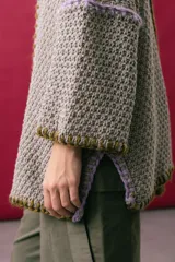 Saco oversize de tejido de punto en color beige, con mangas caídas y detalles de bordado a mano en tonos verde y lila en los bordes y costuras.