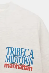 Sudadera de cuello redondo y manga larga, color gris claro, con texto "TRIBECA MIDTOWN manhattan" estampado en azul y rojo en el frente. Acabados en rib.