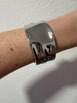 Brazalete rígido de diseño ancho y superficie lisa con efecto metálico pulido y acabado irregular.