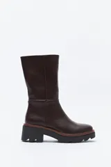 Bota de caña media en cuero sintético color negro, con diseño minimalista y suela robusta dentada con detalle de borde en color marrón.