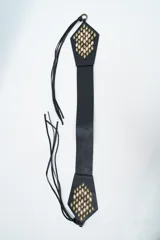 Cinturón negro de cuero sintético con diseño de tiras largas y extremos decorados con apliques metálicos en tonos dorados y bronce.