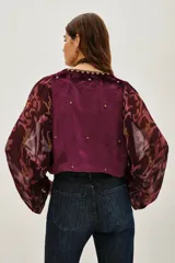 Saco de estilo bohemio confeccionado en terciopelo color violeta, con mangas largas abullonadas de tela fluida estampada. Presenta un panel central bordado con detalles ornamentales y cierre frontal.