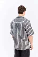 Camisa de manga corta oversize en tejido rústico, con diseño de rayas verticales celestes y blancas, cuello clásico y cierre frontal de botones.